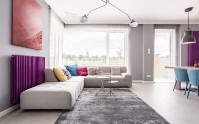 Abstract painting hanging above a purple radiator, and a large sofa with many, colorful pillows in a stylish living room