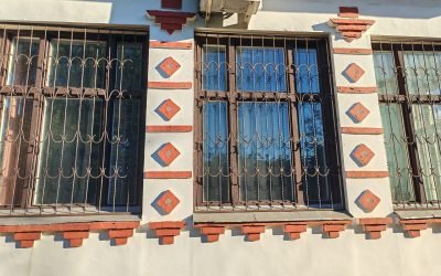 close-up of barred windows with decorative ironwork on a building's facade, framed by red brick accents. The design highlights the combination of security and ornamental architecture in urban structures.